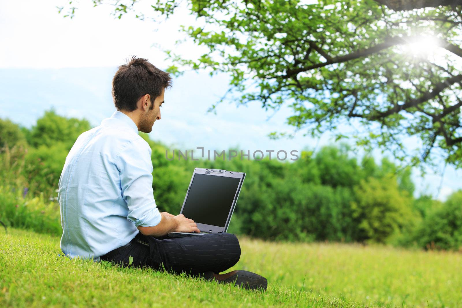 Businessman sitting on the grass is working on laptop