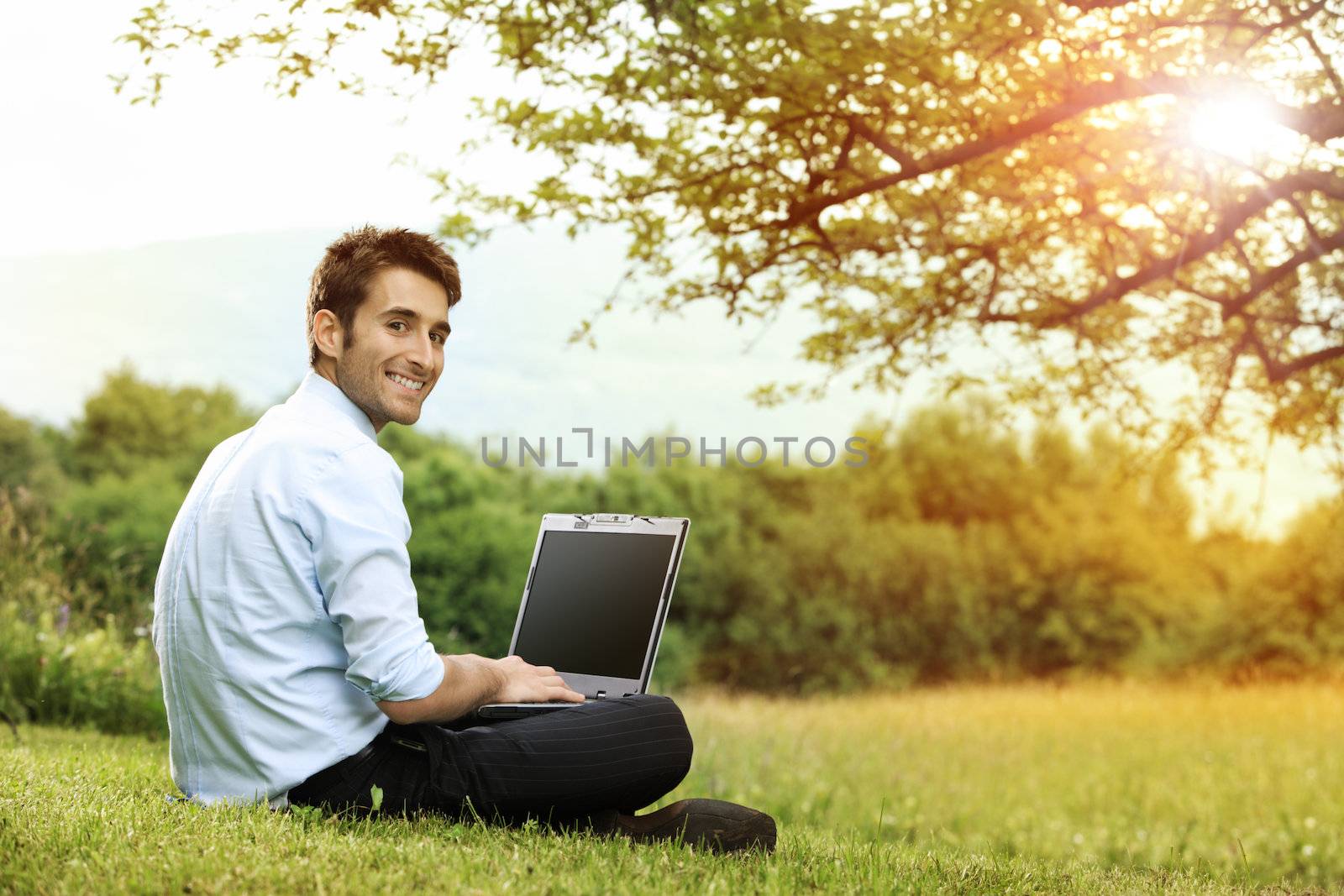 Businessman sitting on the grass is working on laptop