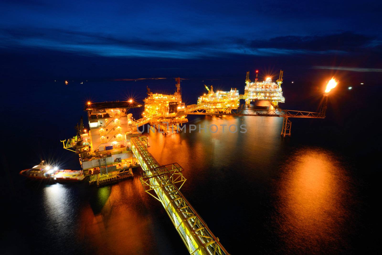 The supply boat is working at large offshore oil rig at night with twilight background