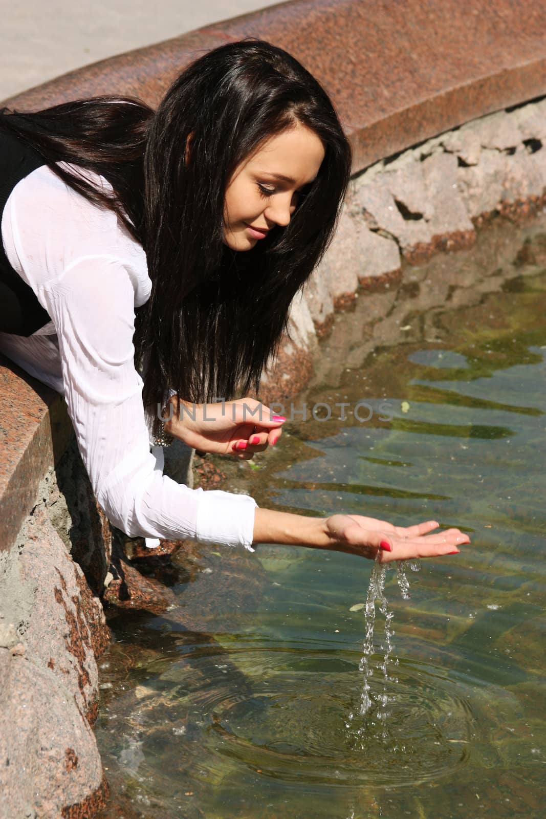 The young beautiful young woman touch fountain hand