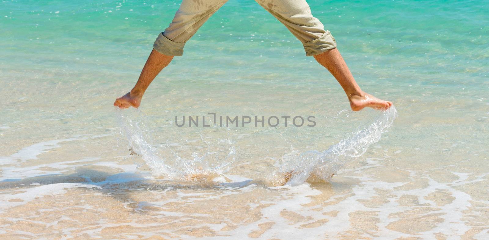 Male legs under clean blue sea water jumping up and splashing water