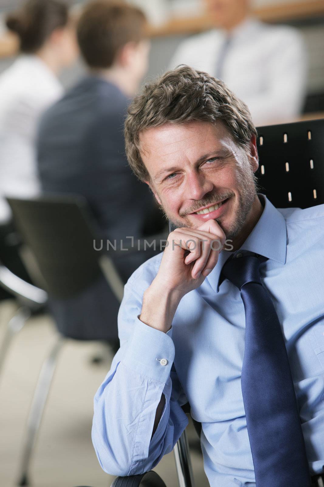 Happy mature businessman with colleagues in the background