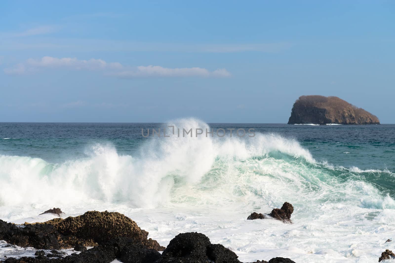 Waves breaking on a stony beach under blue sky and island on background