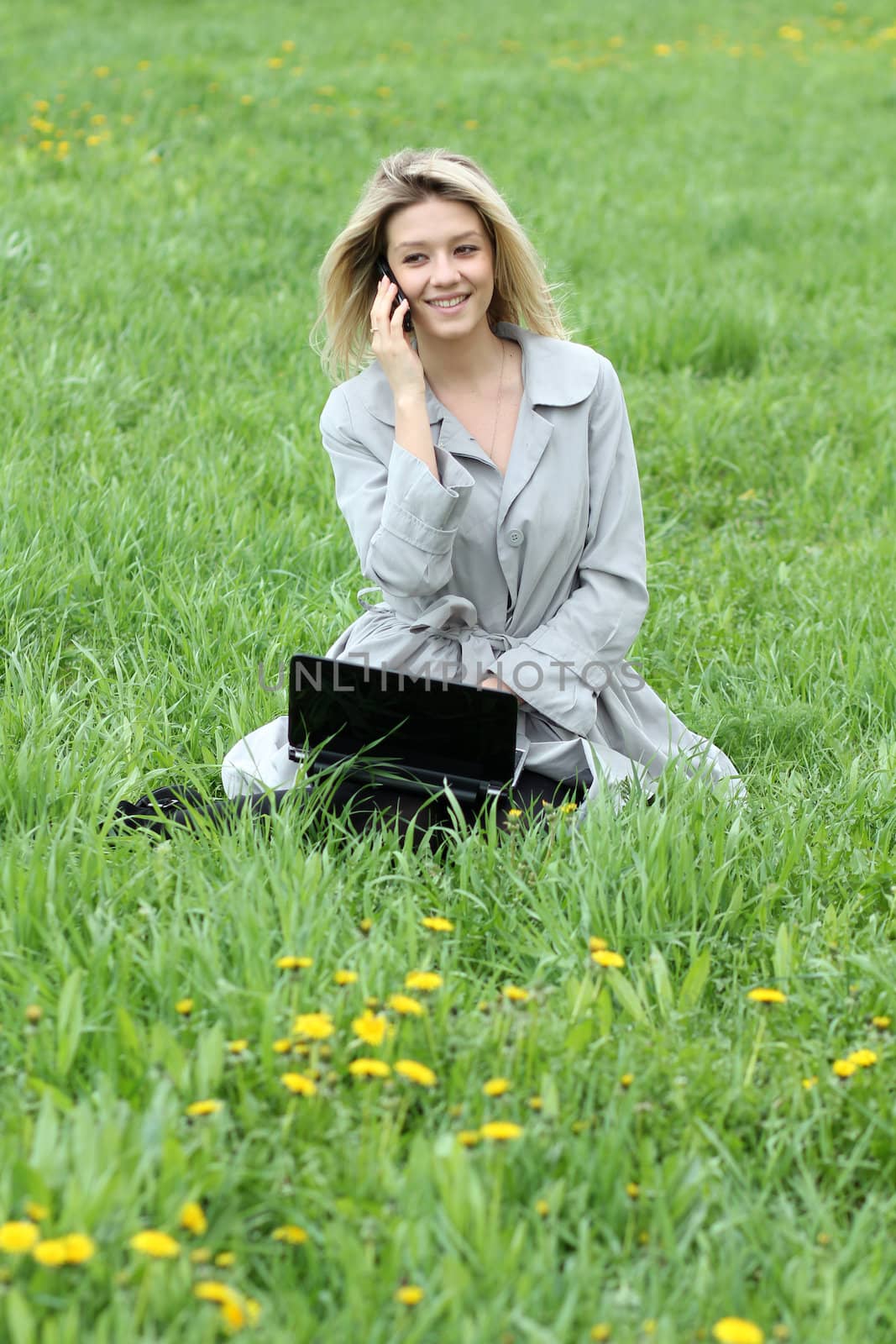 Young blonde girl working on laptop and talking on cell phone