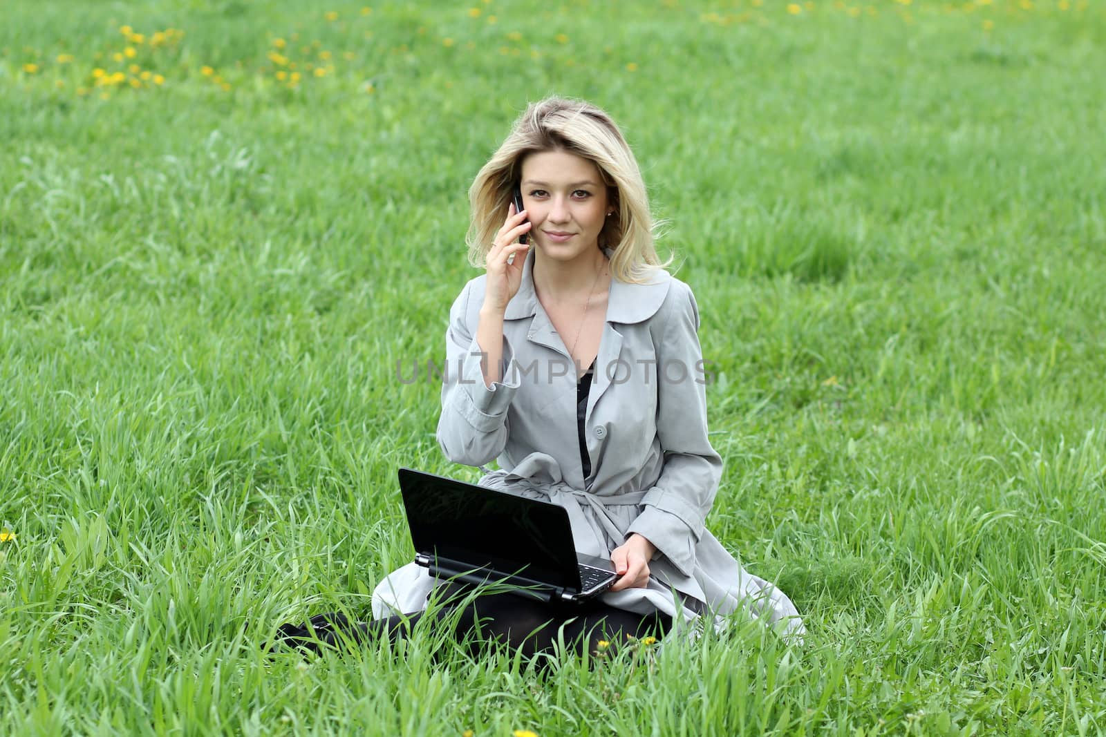 Young blonde girl working on laptop and talking on cell phone