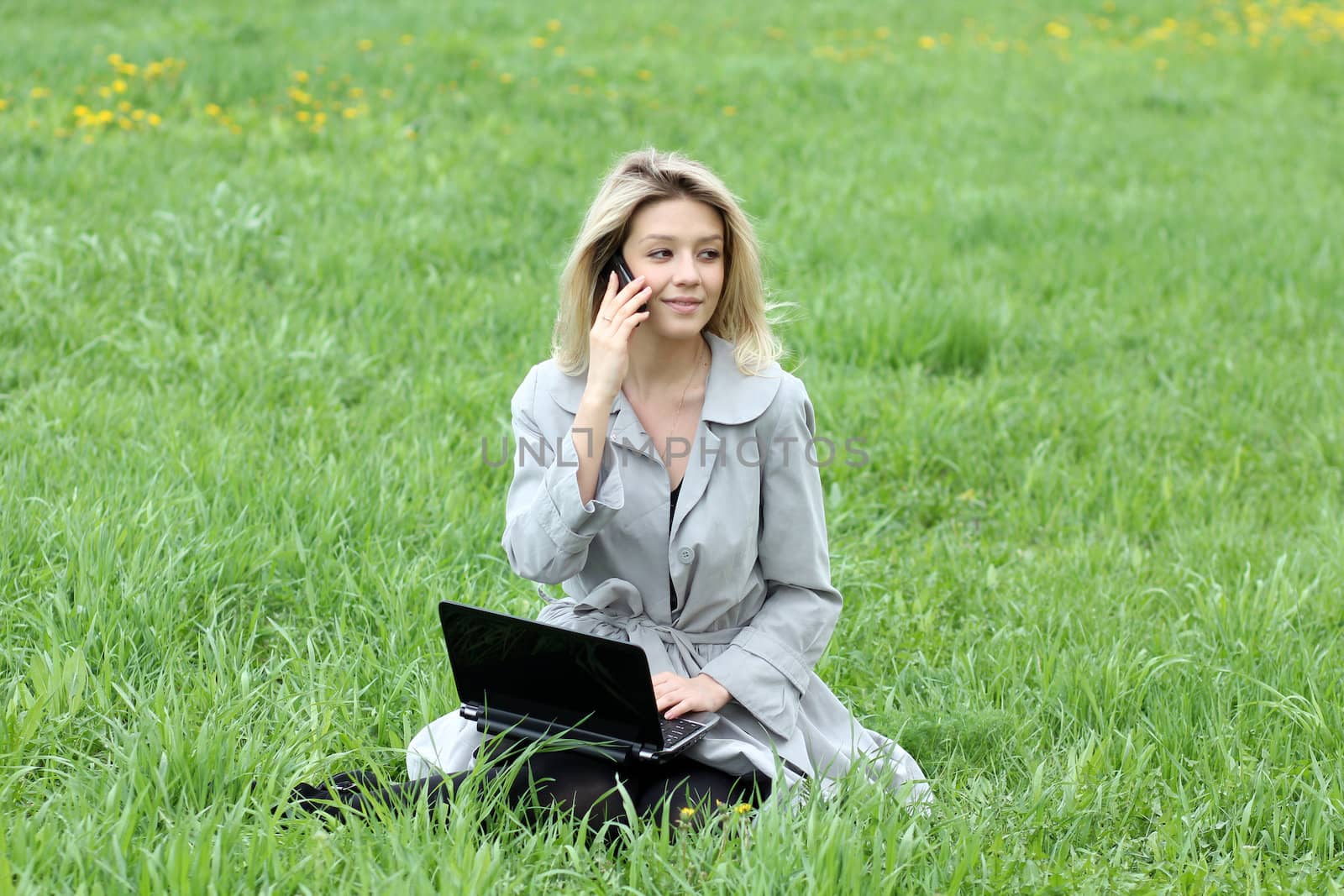 Young blonde girl working on laptop and talking on cell phone