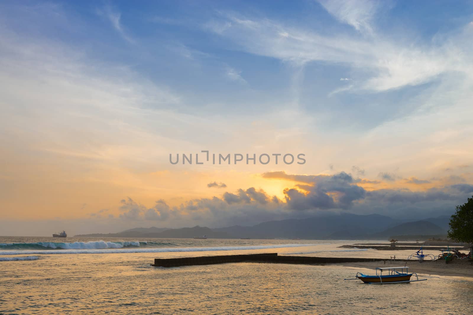 Sunset on a tropical sea shore with breakwaters and boats on Bali in Candidasa, Indonesia