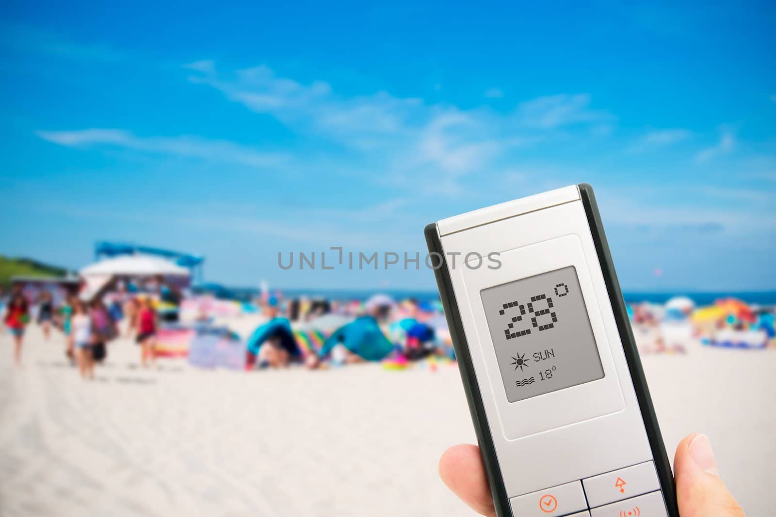 Hand holding electronic thermometer. People on the beach in background