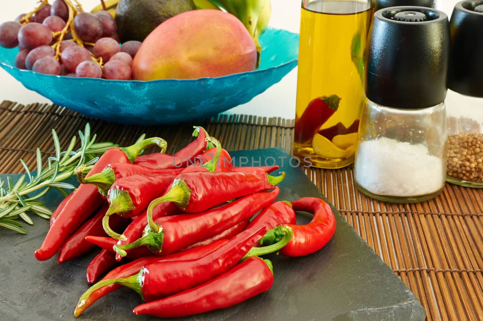Some red hot chili peppers on a slate tray with fuit and other ingredients on the background