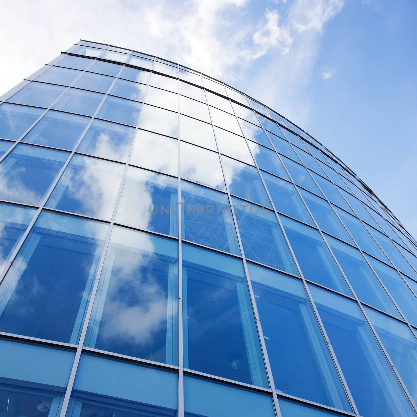 curved facade of modern glass blue office and clouds by ahavelaar