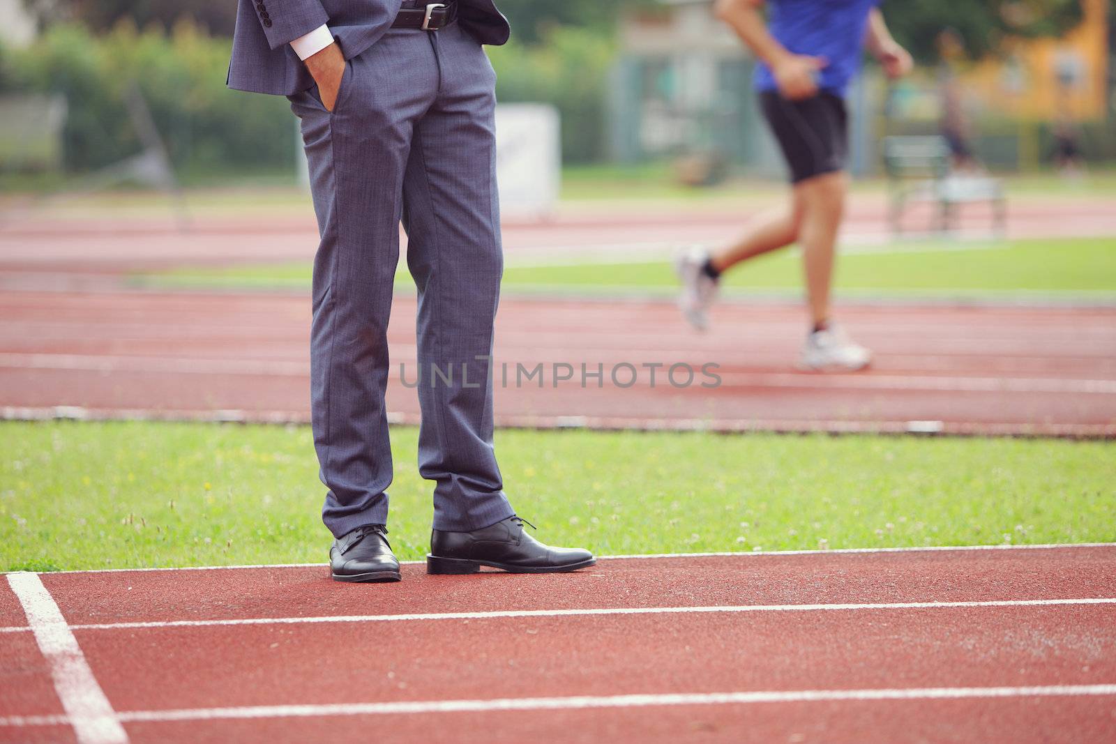 Businessman standing on running track, an athlete is running in the background