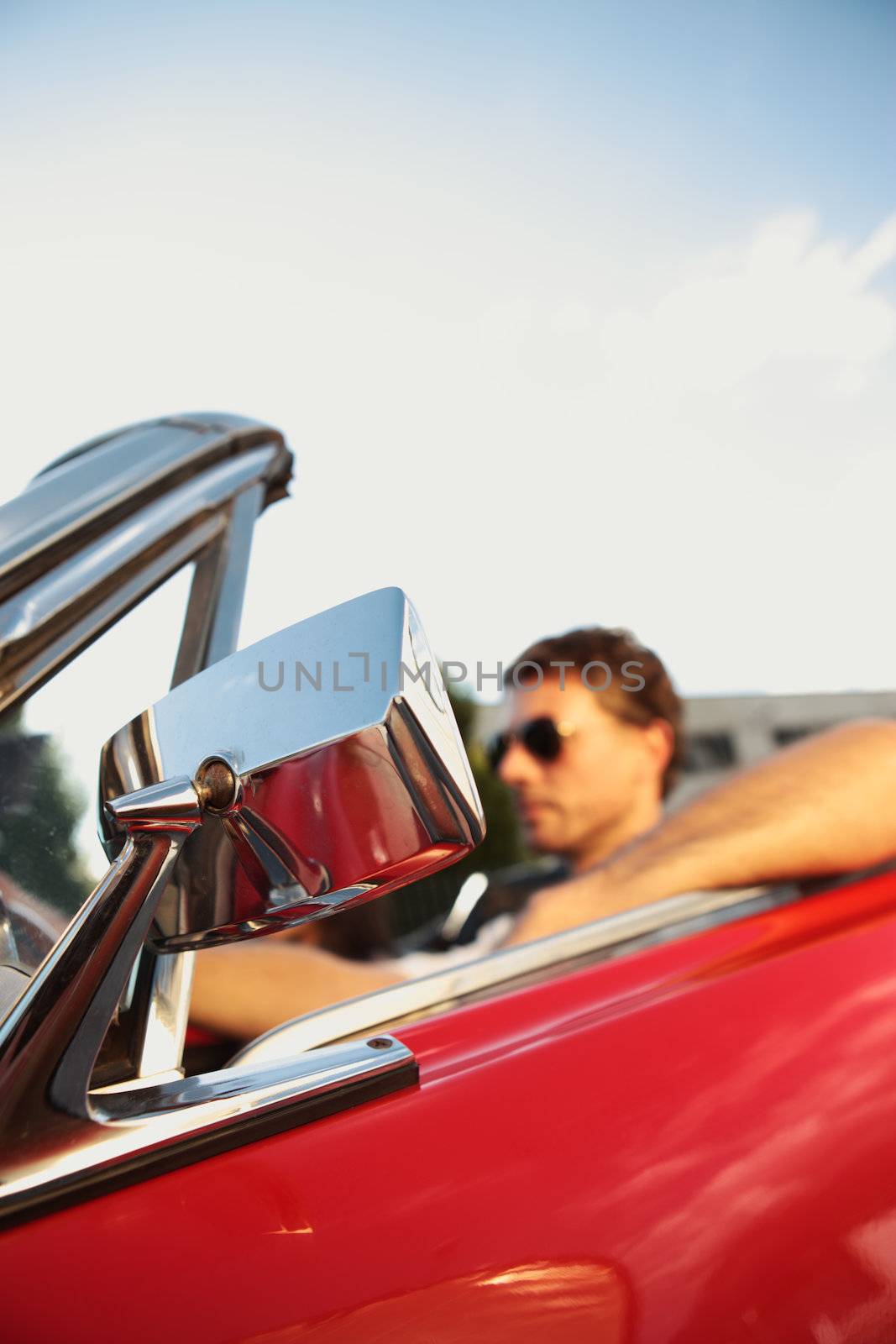 Handsome man driving a convertible car, focus on Rear-View Mirror