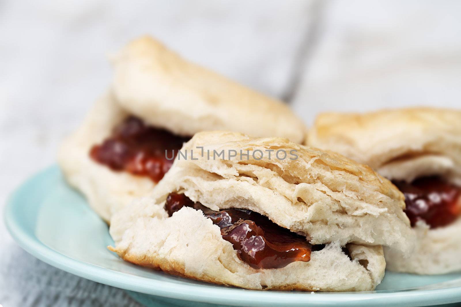 Closeup of freshly baked scones at the breakfast table with strawberry jam. Extreme shallow depth of field with selective focus.