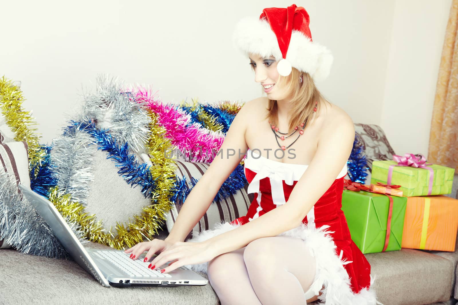 Smiling lady sitting indoors in Santa Claus costume making online Christmas greeting