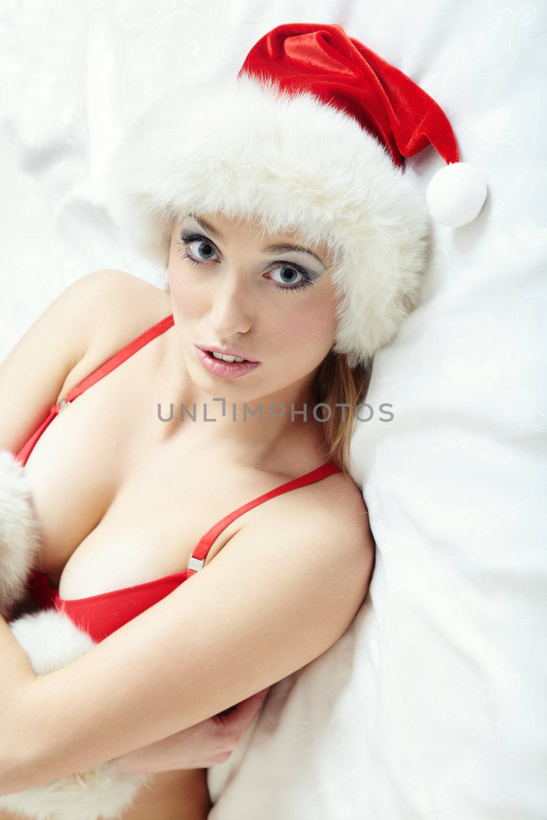 Sexy smiling lady in the red camisole and furry Santa Claus hat laying indoors