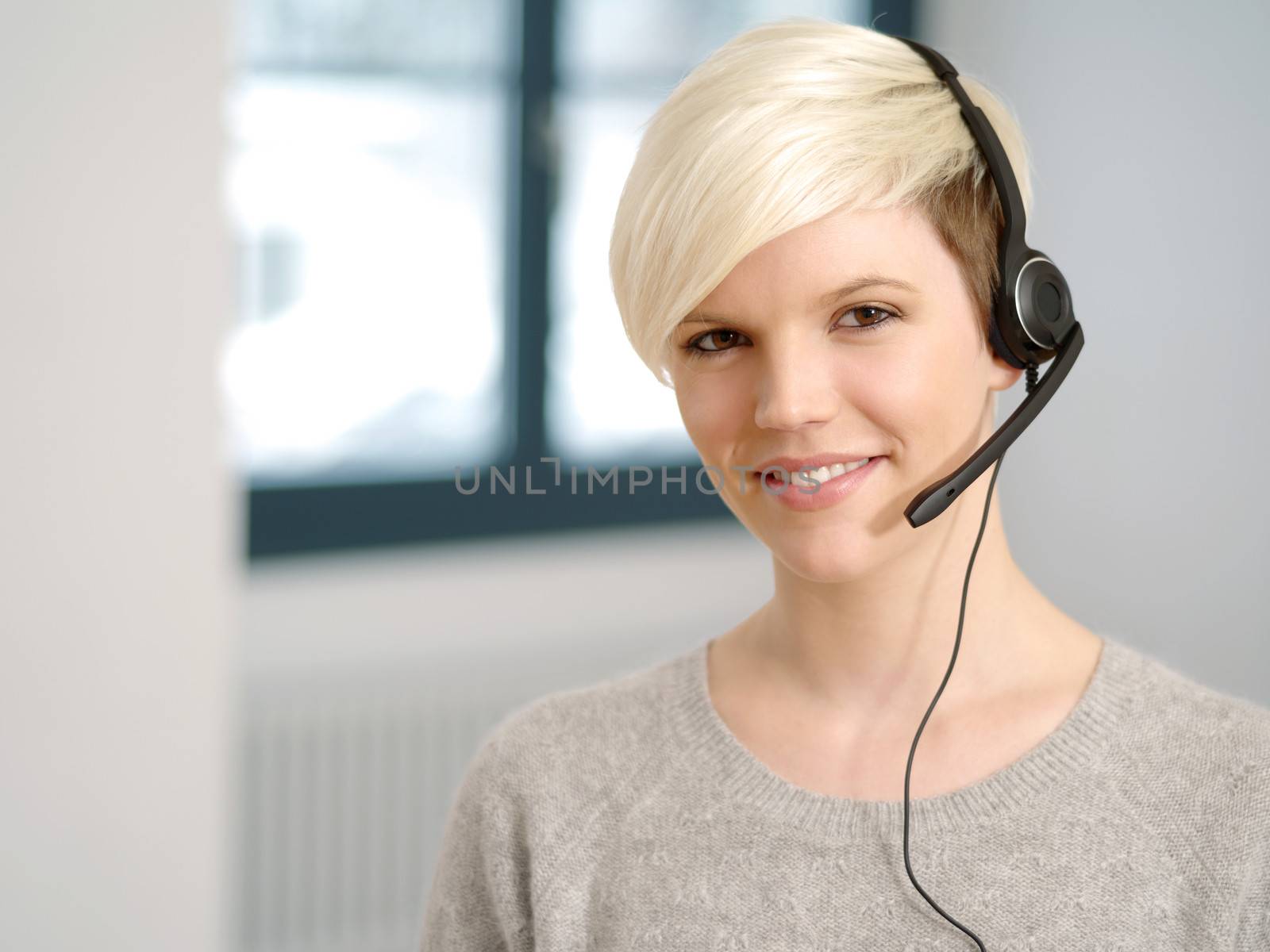 Photo of a cute young call center female with short blond hair and big smile wearing a headset.