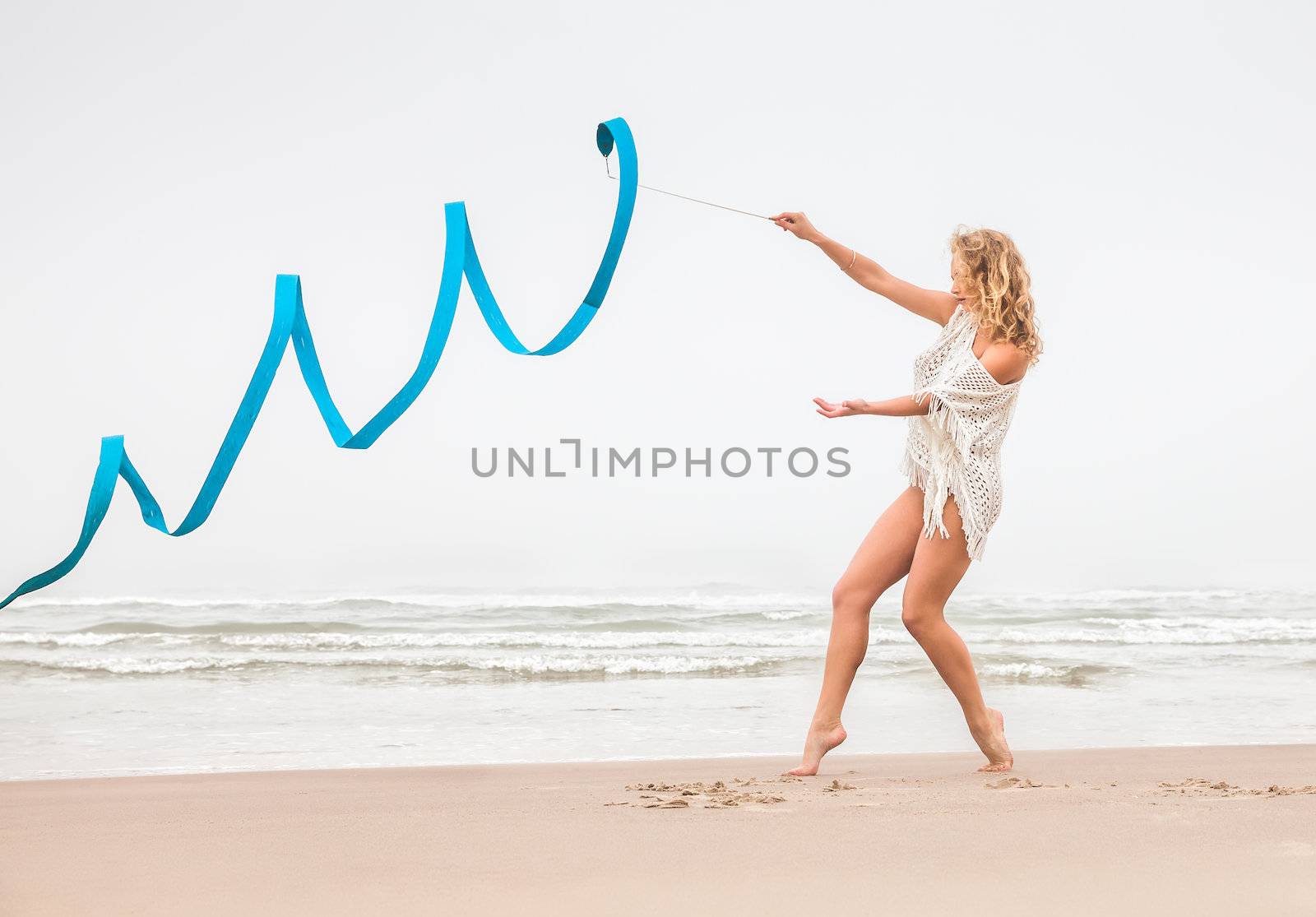 Young beautiful gymnast woman dance with ribbon on the beach at foggy day