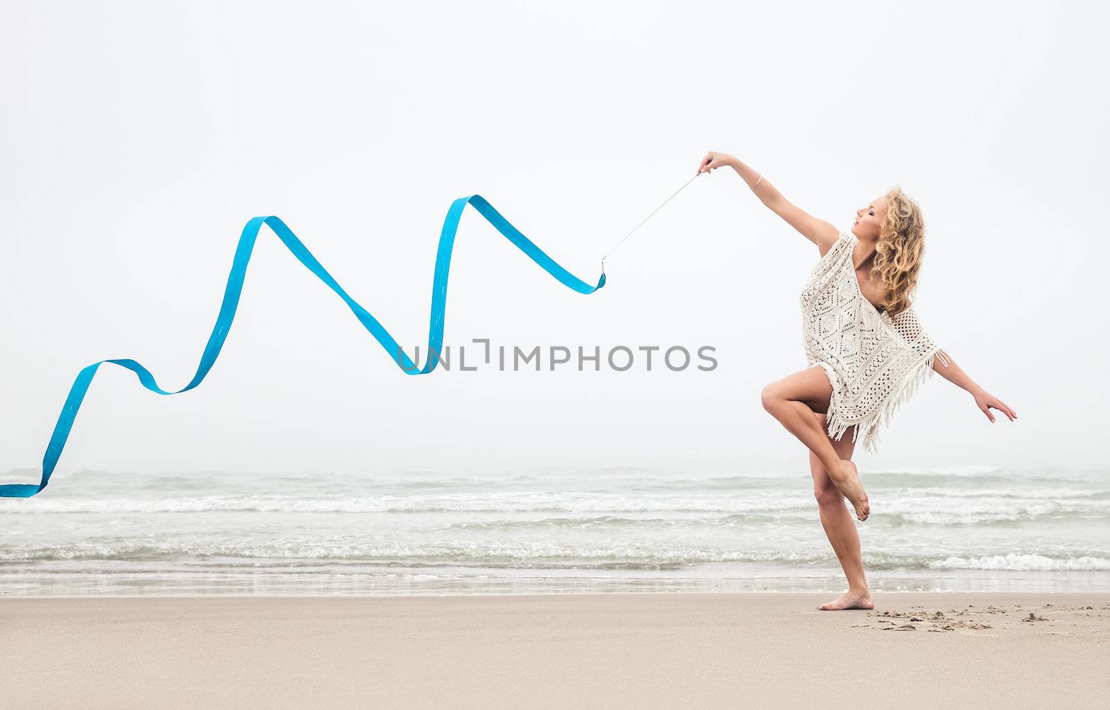 Young beautiful gymnast woman dance with ribbon on the beach at foggy day