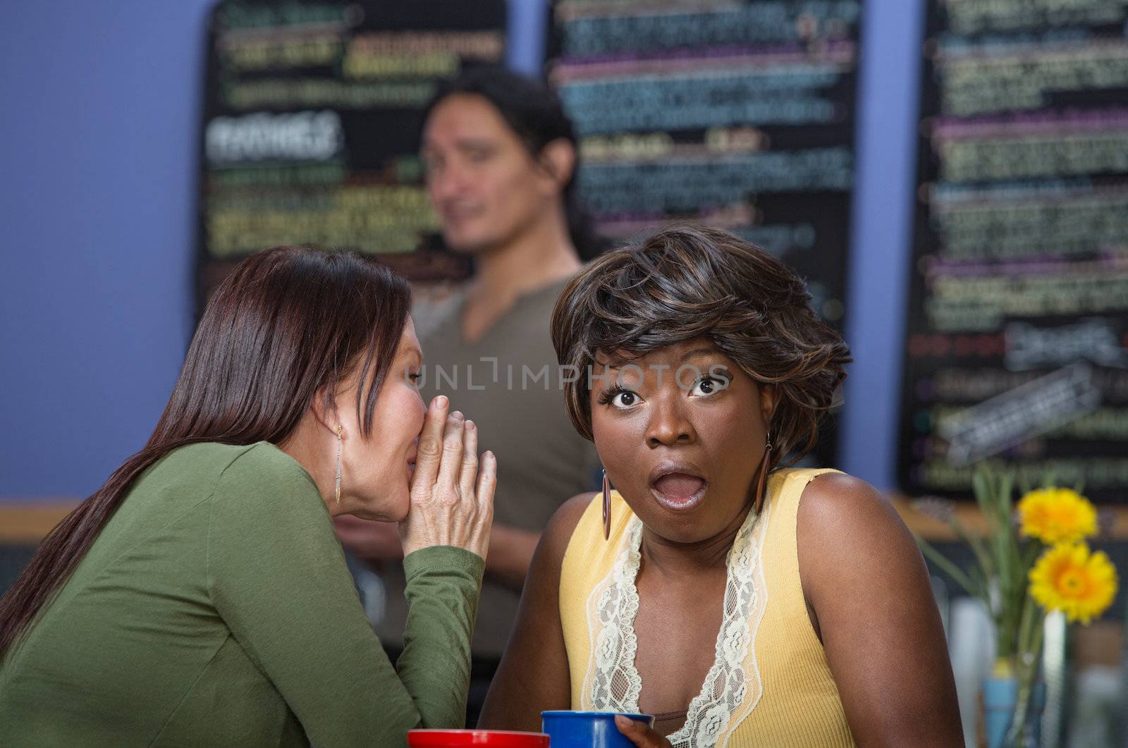 Woman whispering to another in coffee house