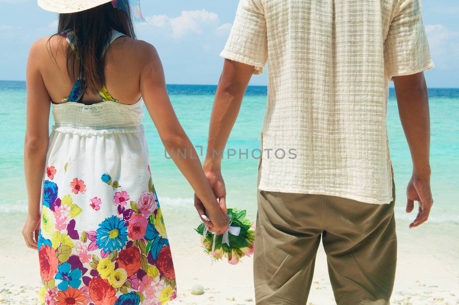 Young couple holding hands on tropical beach.