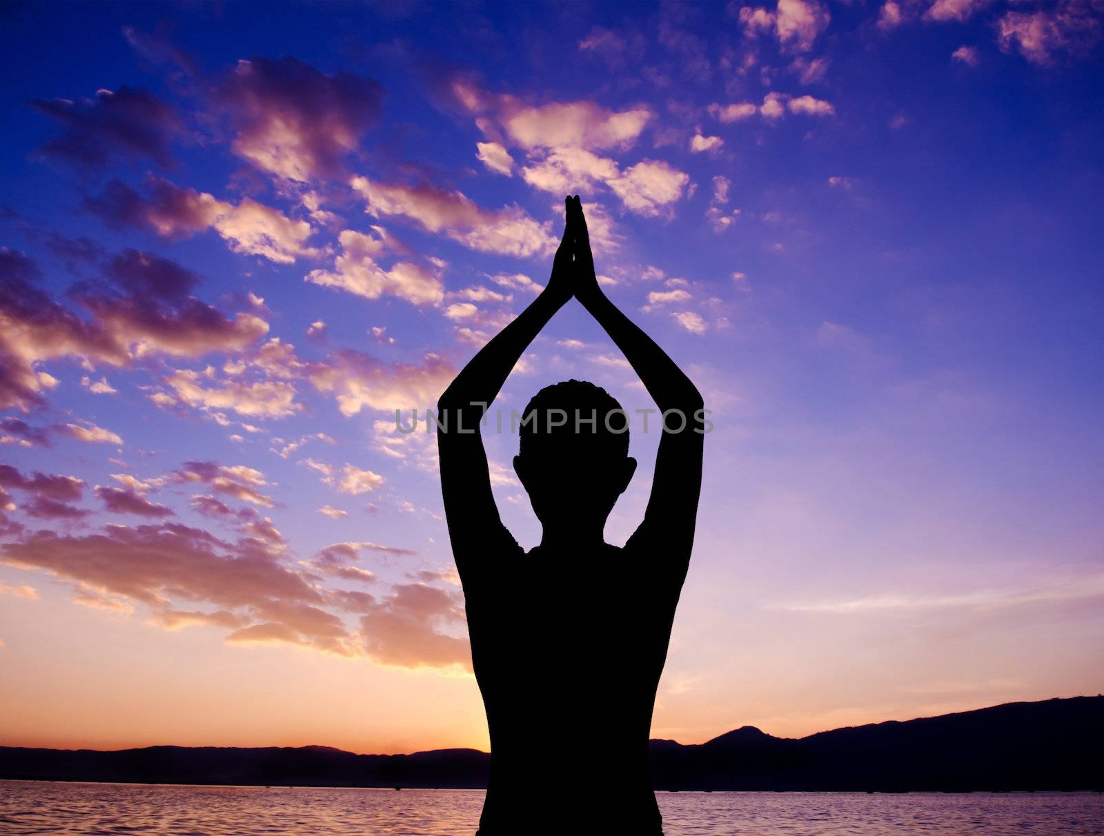 Silhouette of woman doing yoga meditation during sunset with natural golden sunlight at outdoor beach.