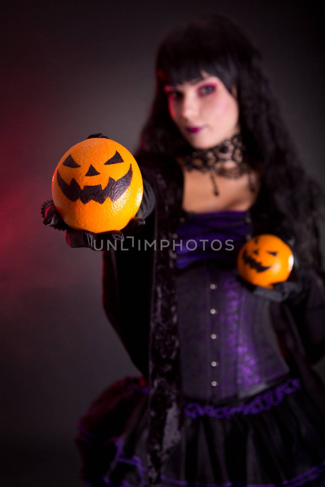 Beautiful witch holding Jack lantern oranges, selective focus on fruits 