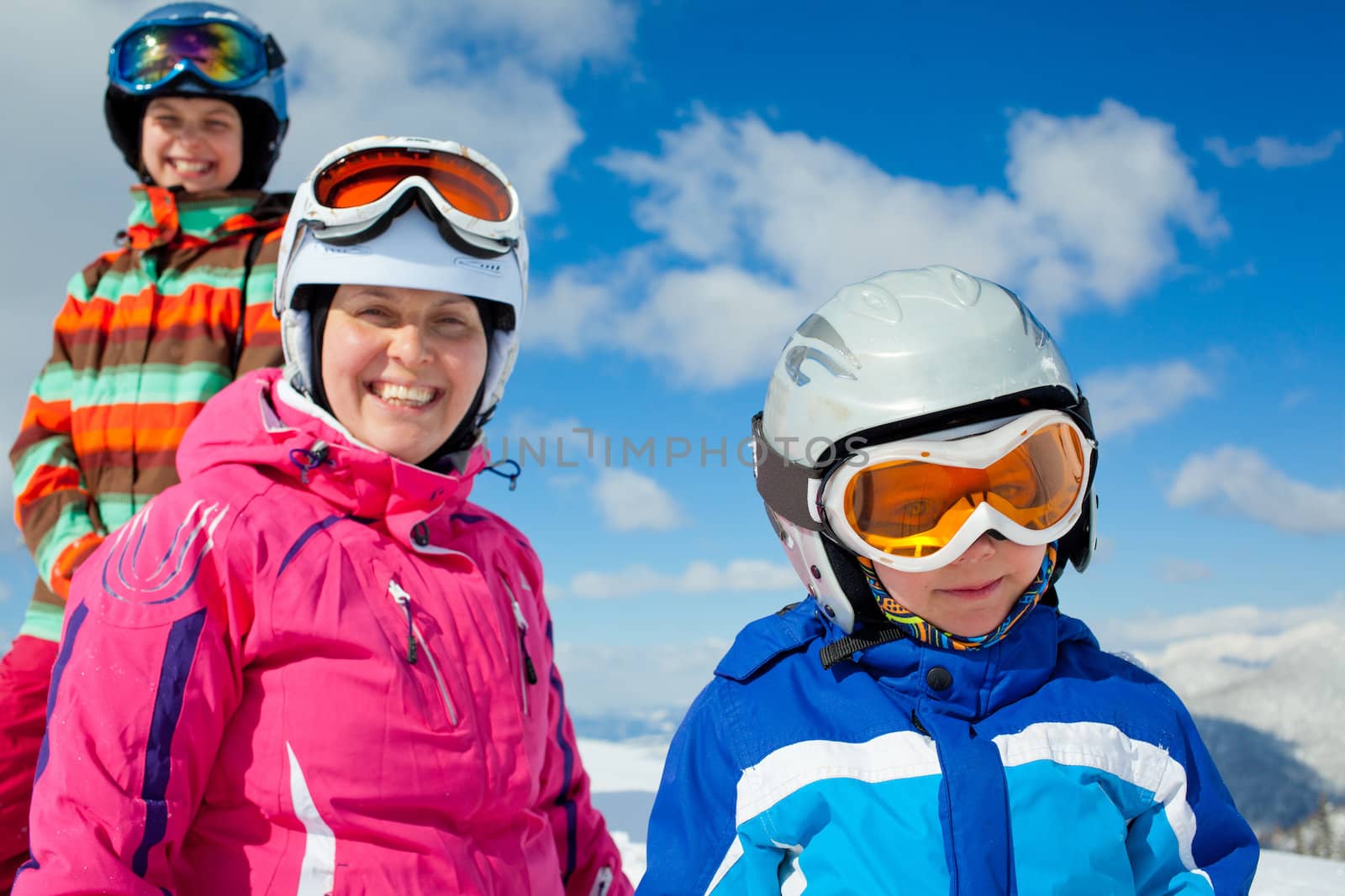 Skiing, winter, family - smiling boy in ski goggles and a helmet with his mother and sister in winter resort