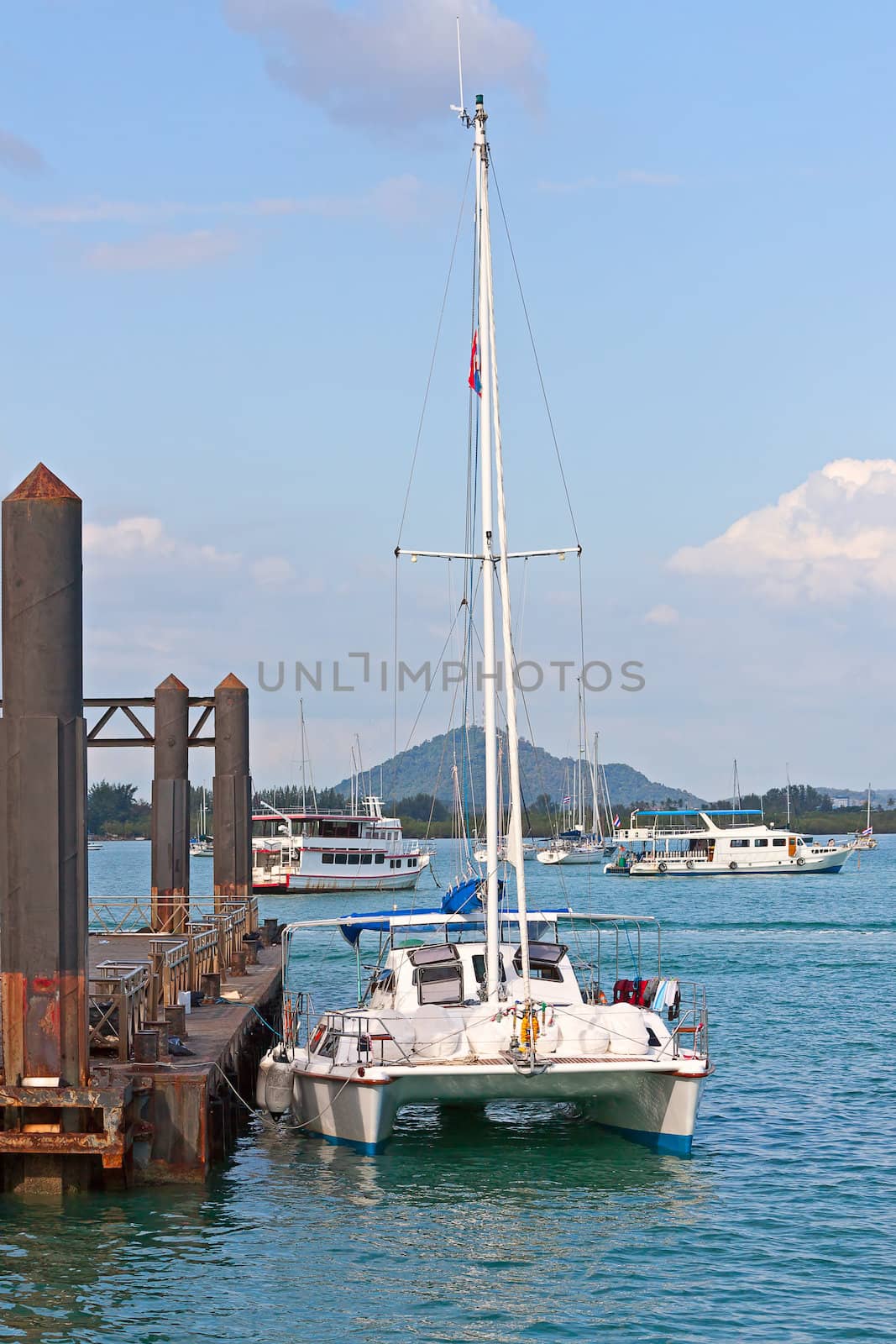 Yacht at berth in background of ships and blue sky, Thailand.
