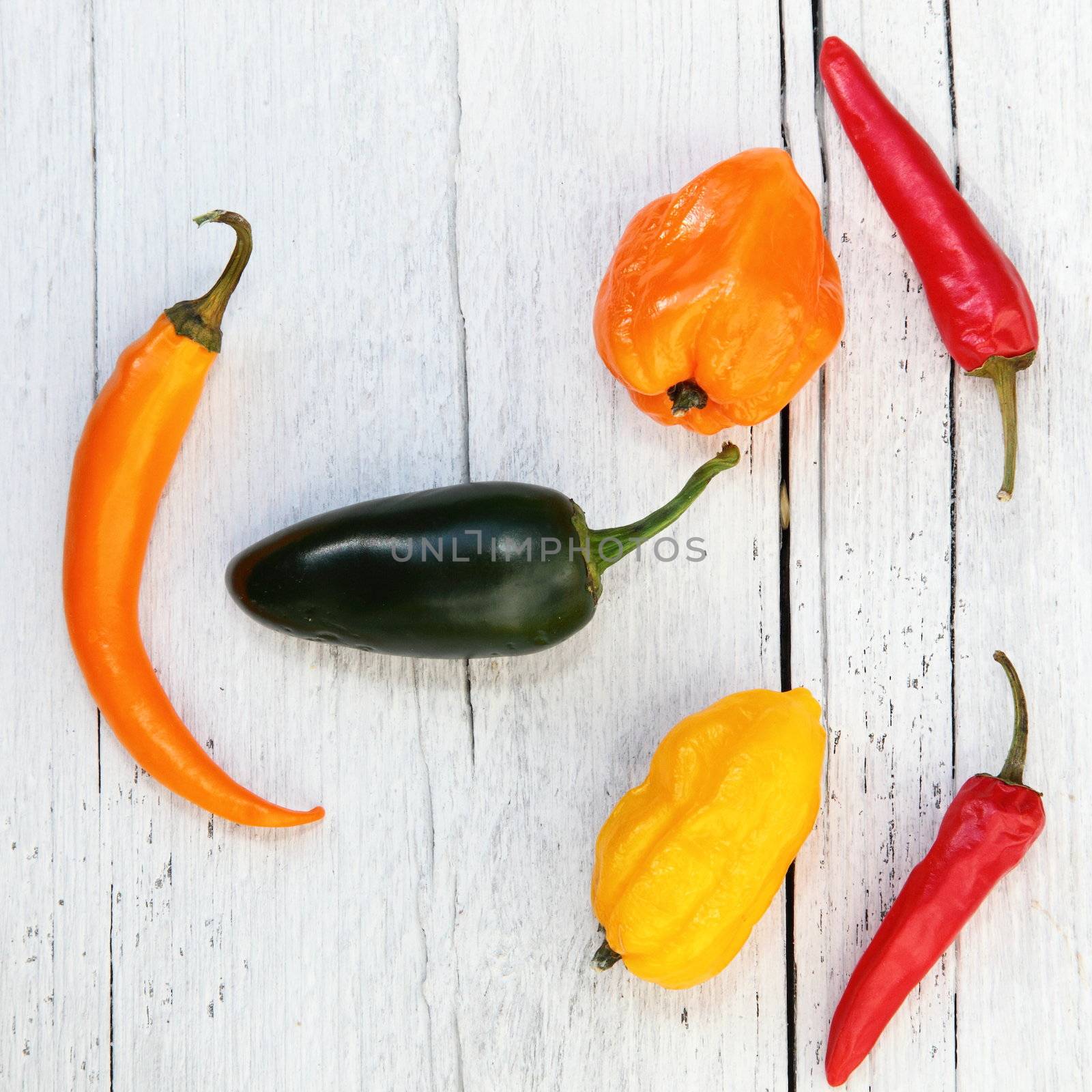 Colourful fresh whole bell and chilli peppers arranged on a painted wooden textured background in the form of a face orientated sideways