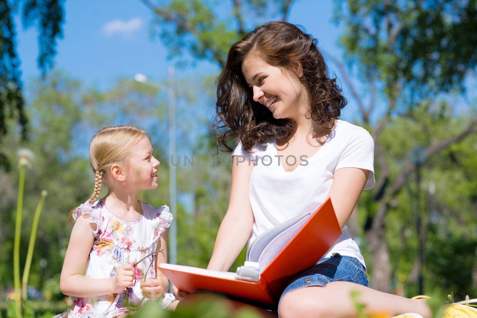 girl with the teacher reading a book together in the summer park