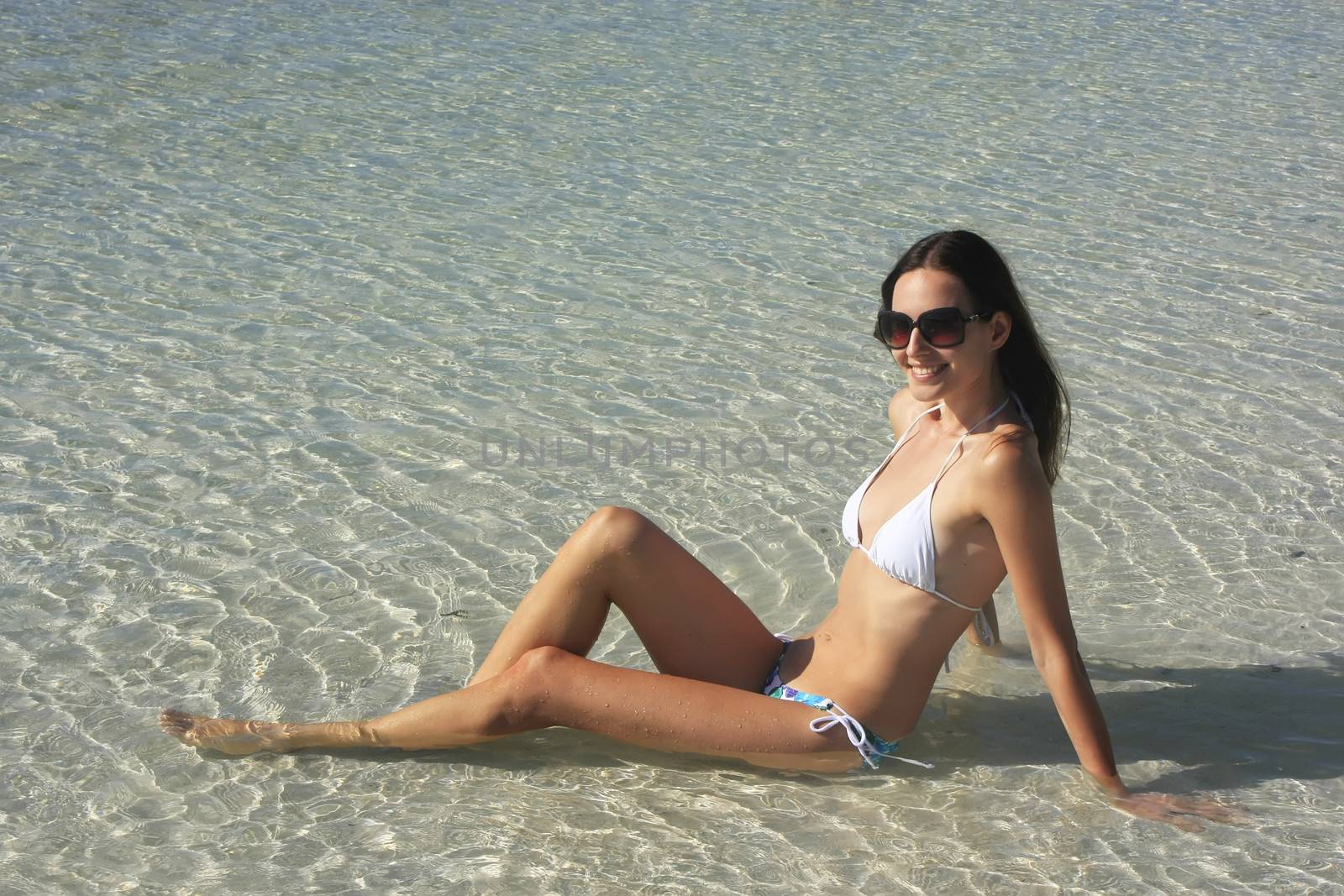 Young woman in bikini sitting in clear shallow water