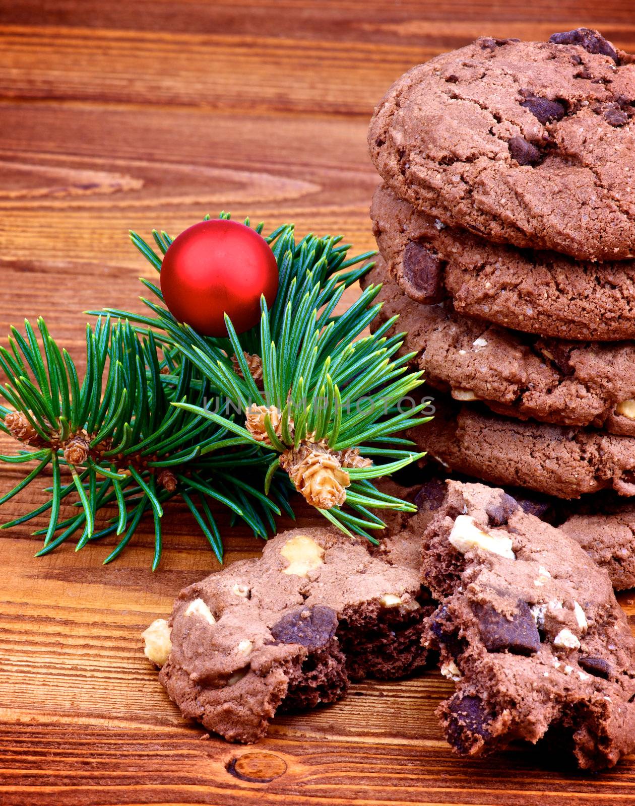 Stack of Delicious Christmas Chocolate Cookies with Green Spruce Branch and Red Bauble closeup on Wooden background 