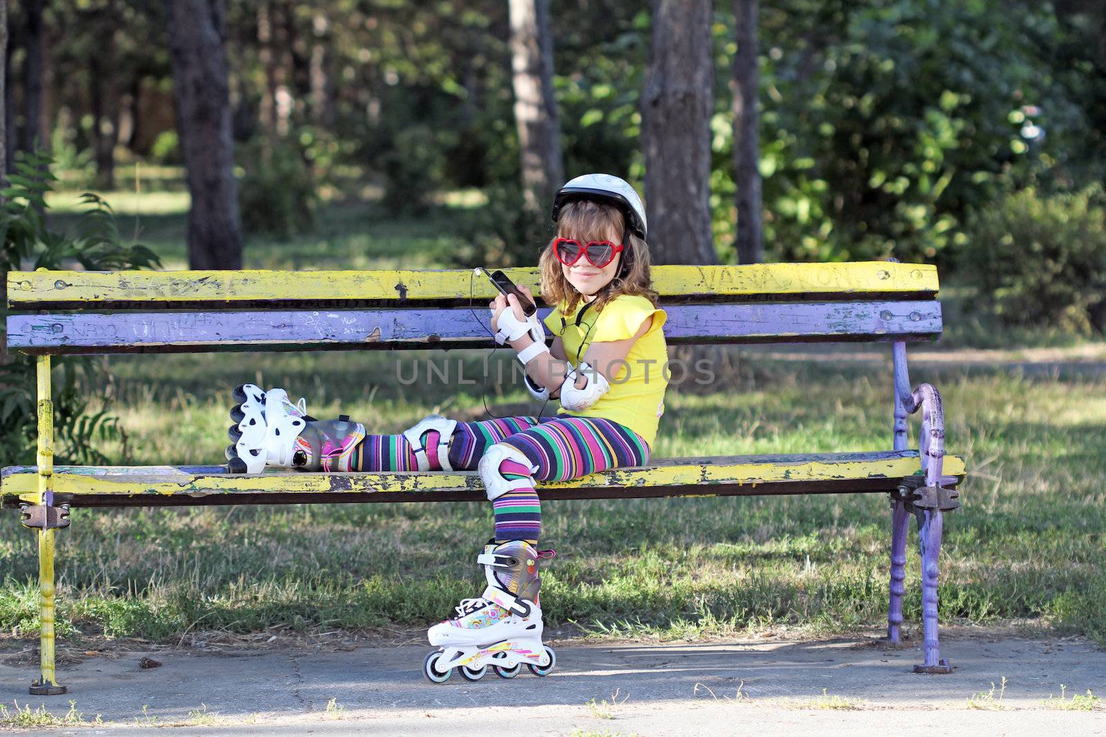 little girl with roller skates sitting on bench and listening mu by goce