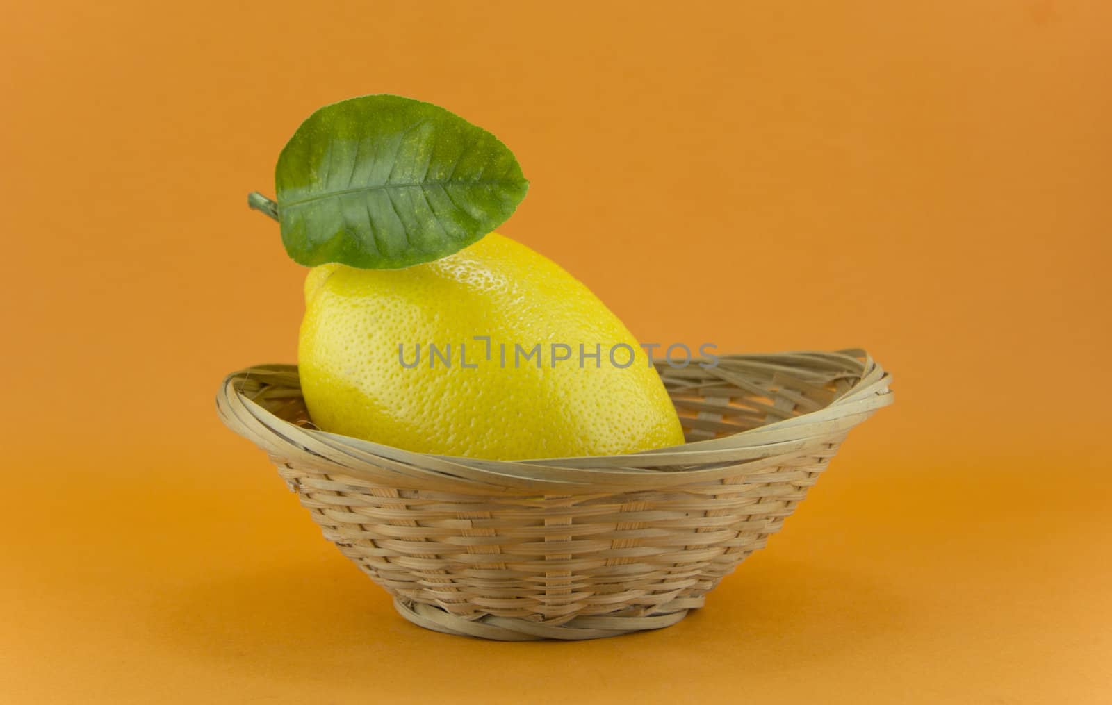 yellow ripe lemon with leaf over the orange background
