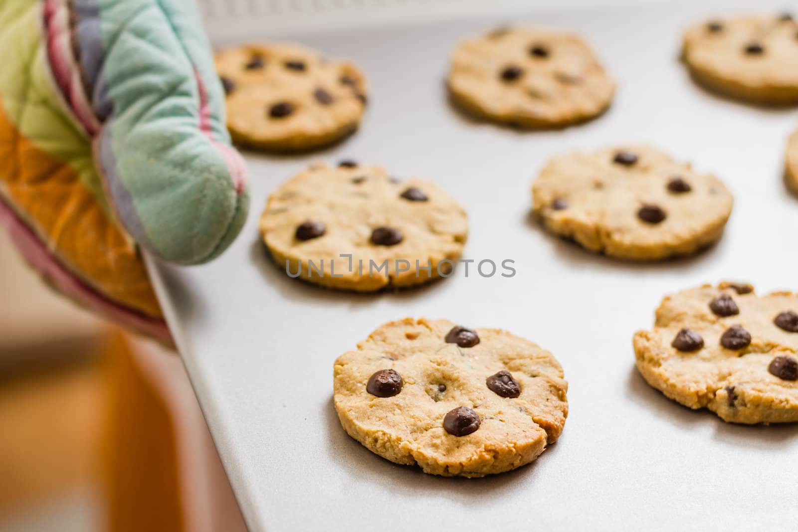 Woman holding a tray with baked cookies with kitchen gloves by doble.d