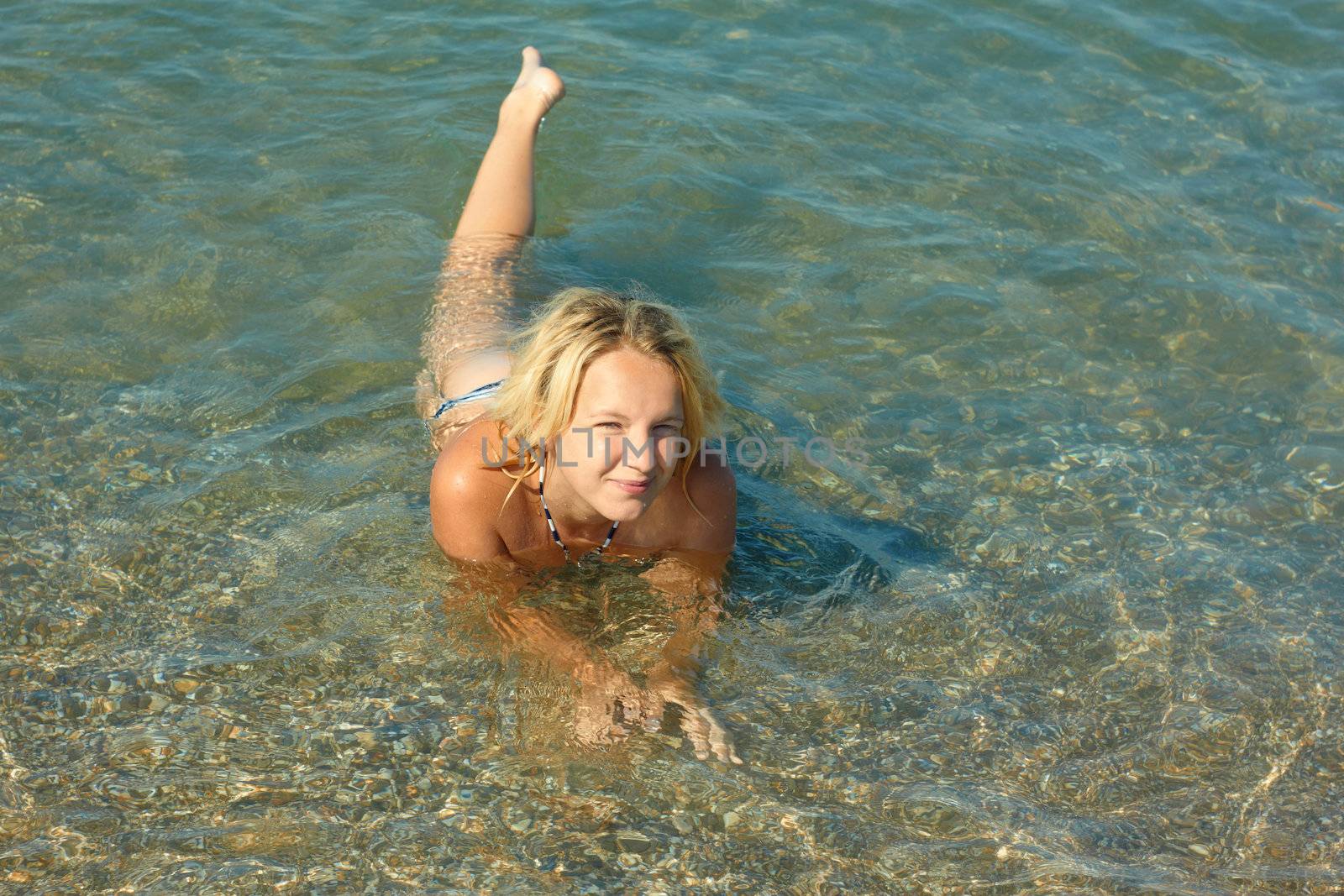 Beautiful smiling teenage girl lying in the shallow coastal sea water with pebbly bottom