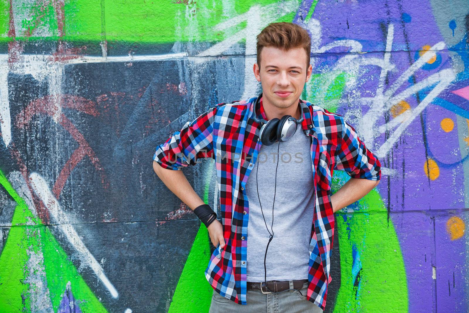 Portrait of happy teens boy with headphones near painted wall