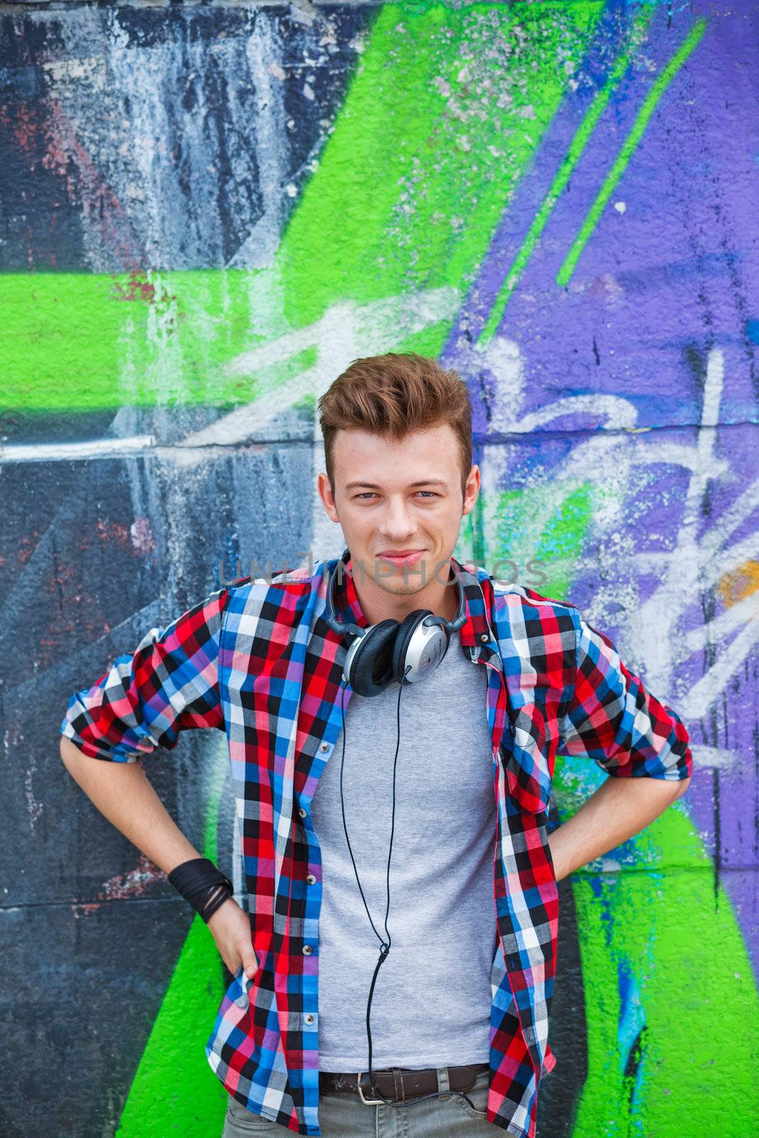 Portrait of happy teens boy with headphones near painted wall. Vertical view