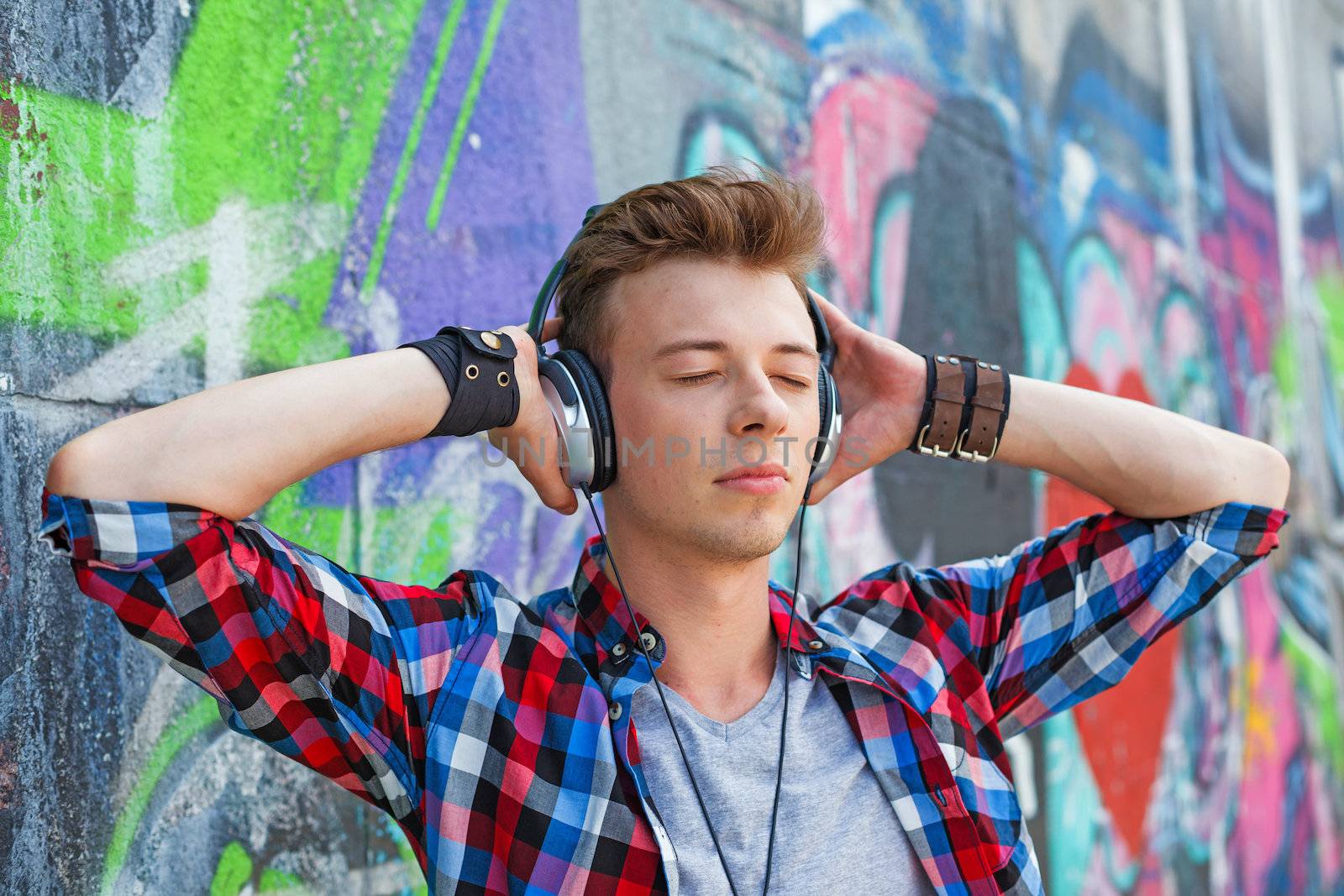 Close-up portrait of happy teens boy with headphones near painted wall listening to music