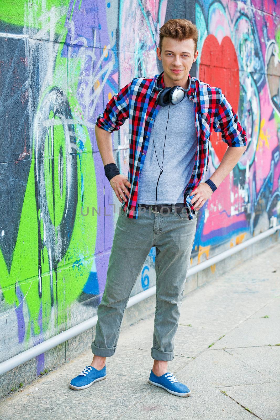 Happy teens boy with headphones near painted wall. Vertical view