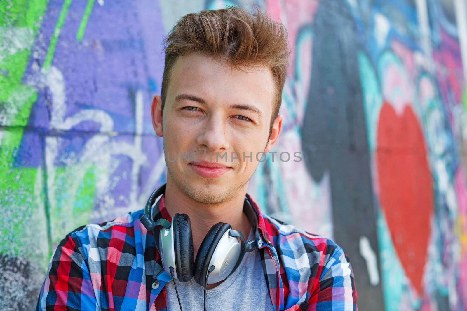 Close-up portrait of happy teens boy with headphones near painted wall listening to music