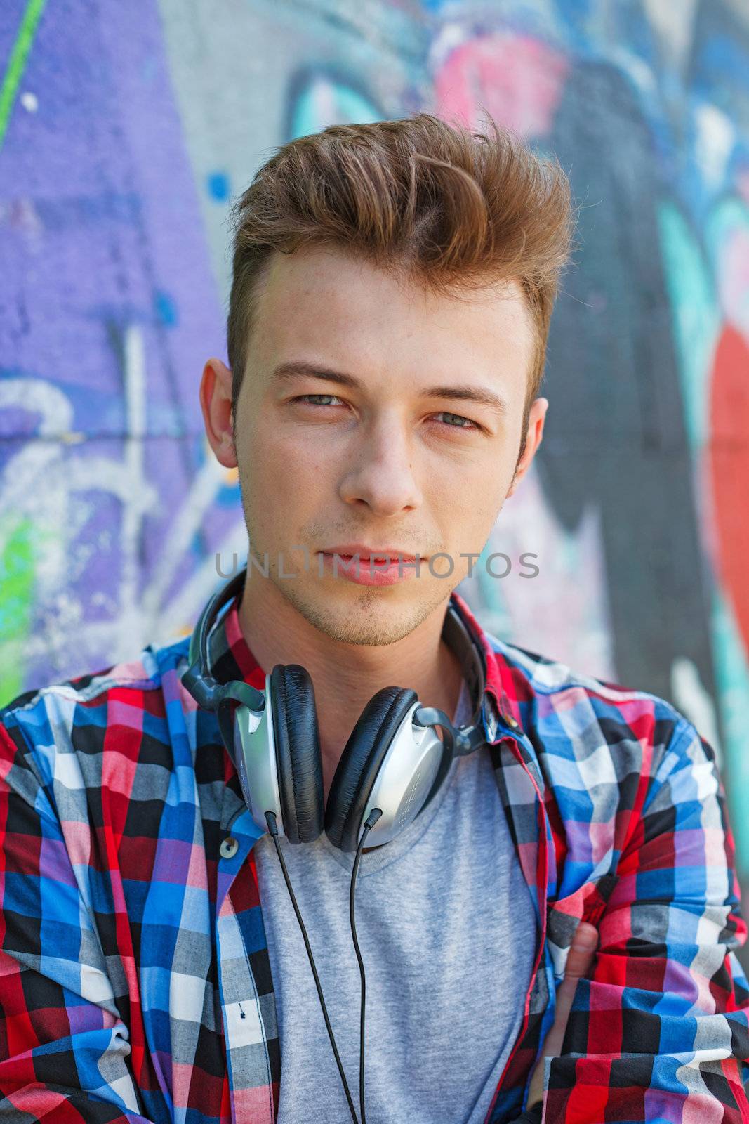 Close-up portrait of happy teens boy with headphones near painted wall listening to music. Vertical view