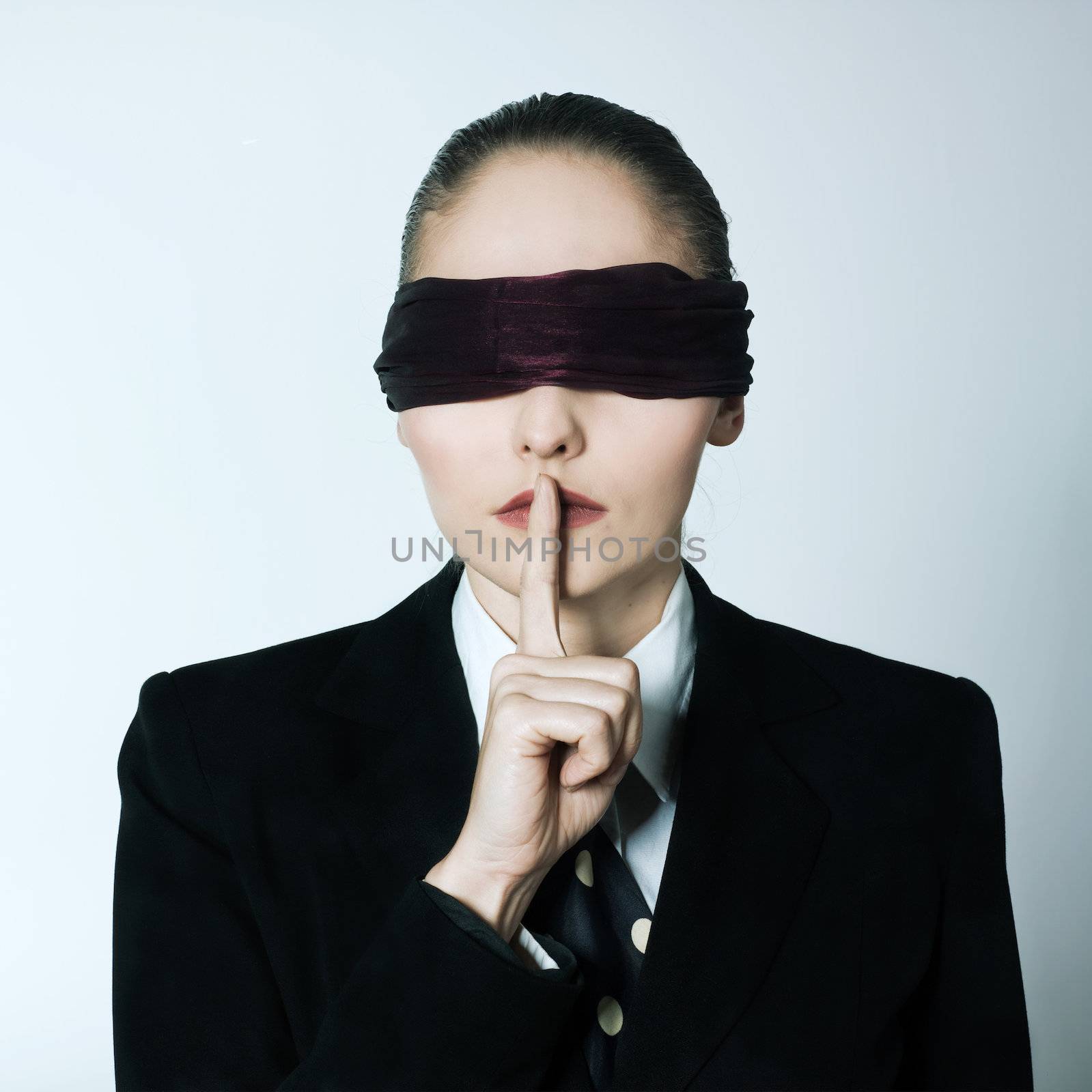 studio shot portrait  young blindfold business woman hushing finger on lips