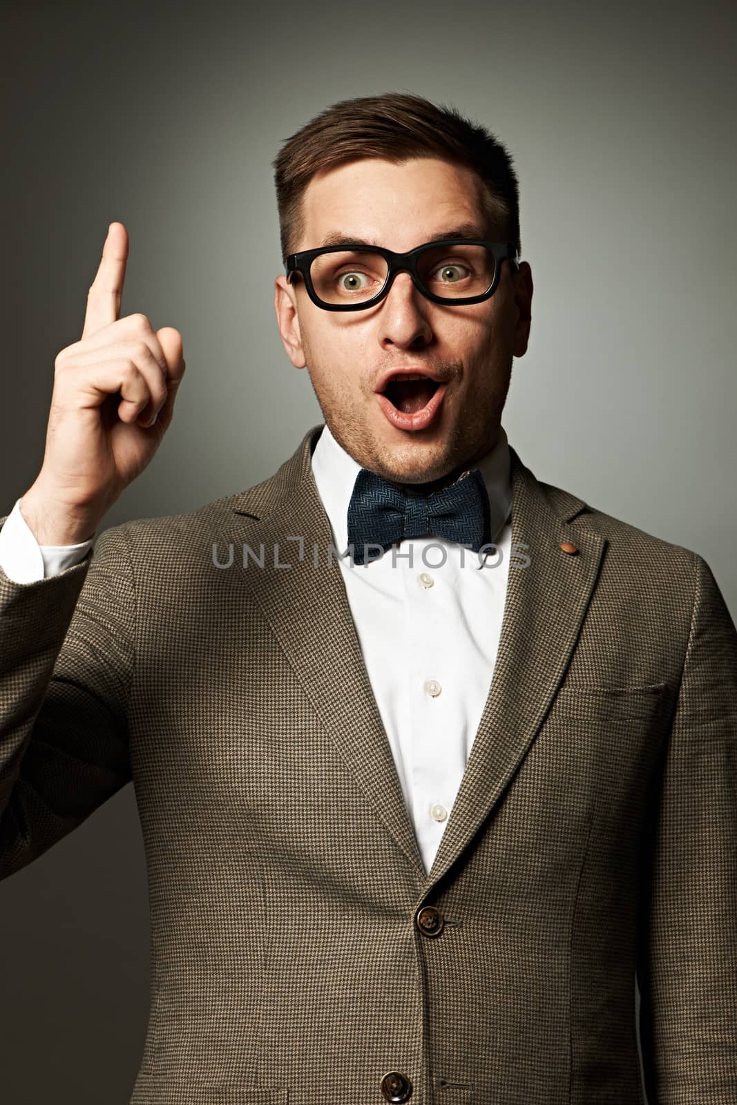 Confident nerd in eyeglasses and bow tie against grey background