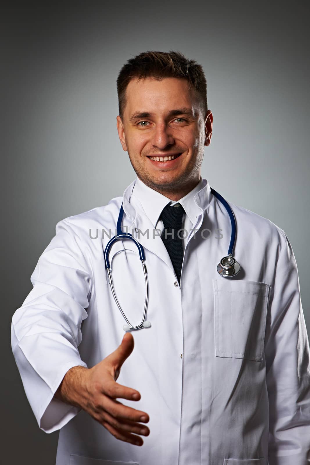 Medical doctor with stethoscope giving hand for handshaking against grey background 