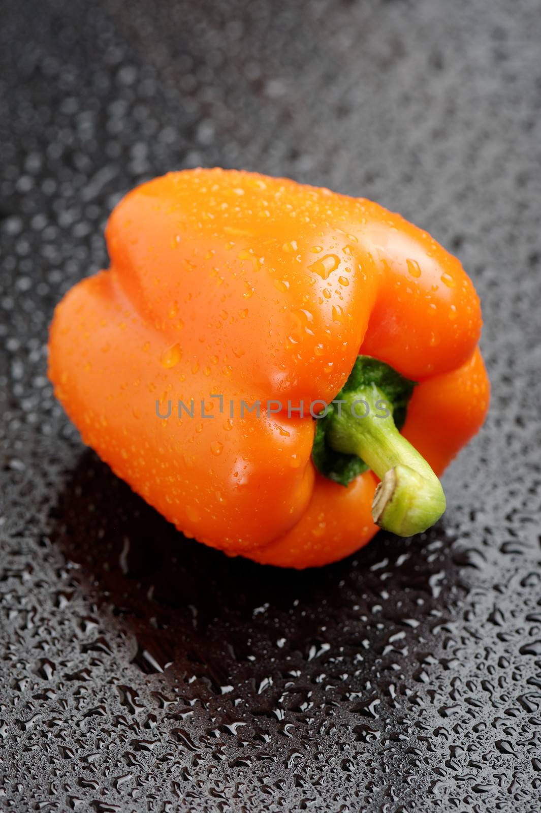Orange bell pepper on black table after rain