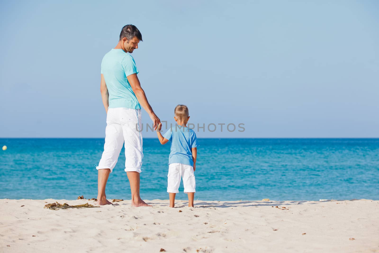 Back view of the father and son watching at the sea on tropical white sand beach