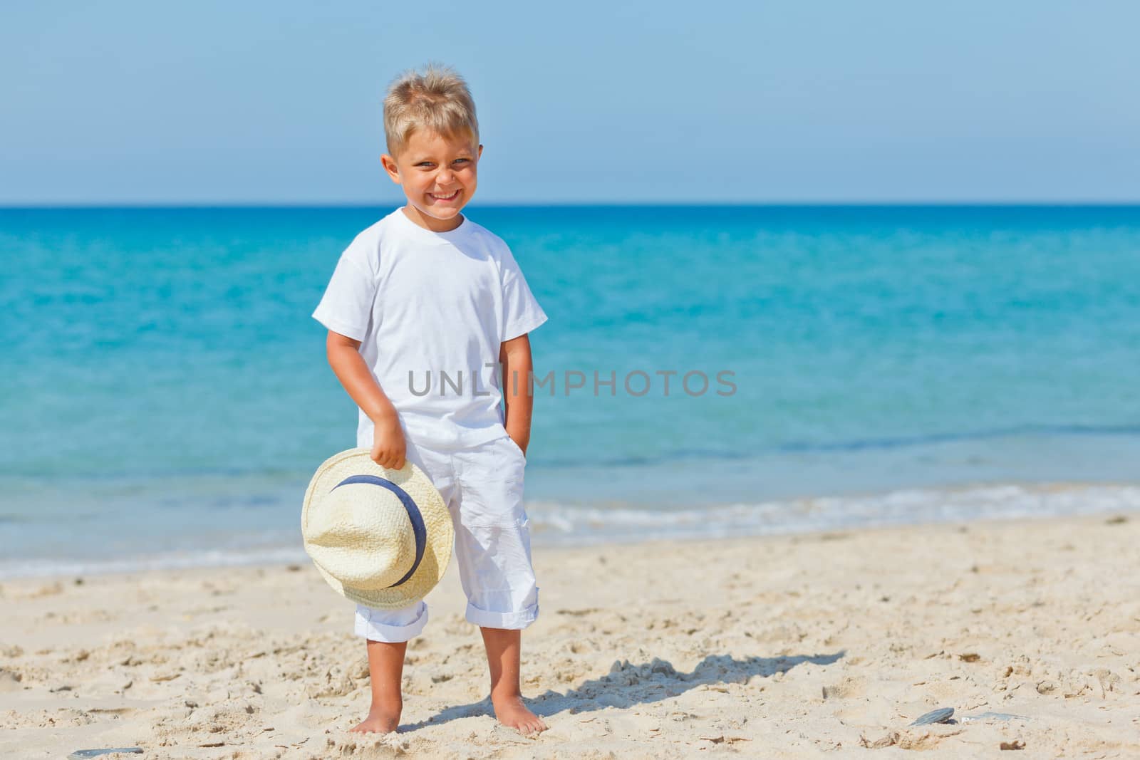 Smiling cute boy with a sun hat at the tropical beach.