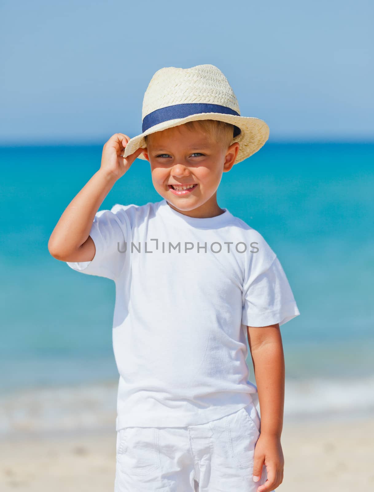 Smiling cute boy in a sun hat at the tropical beach. Vertical view