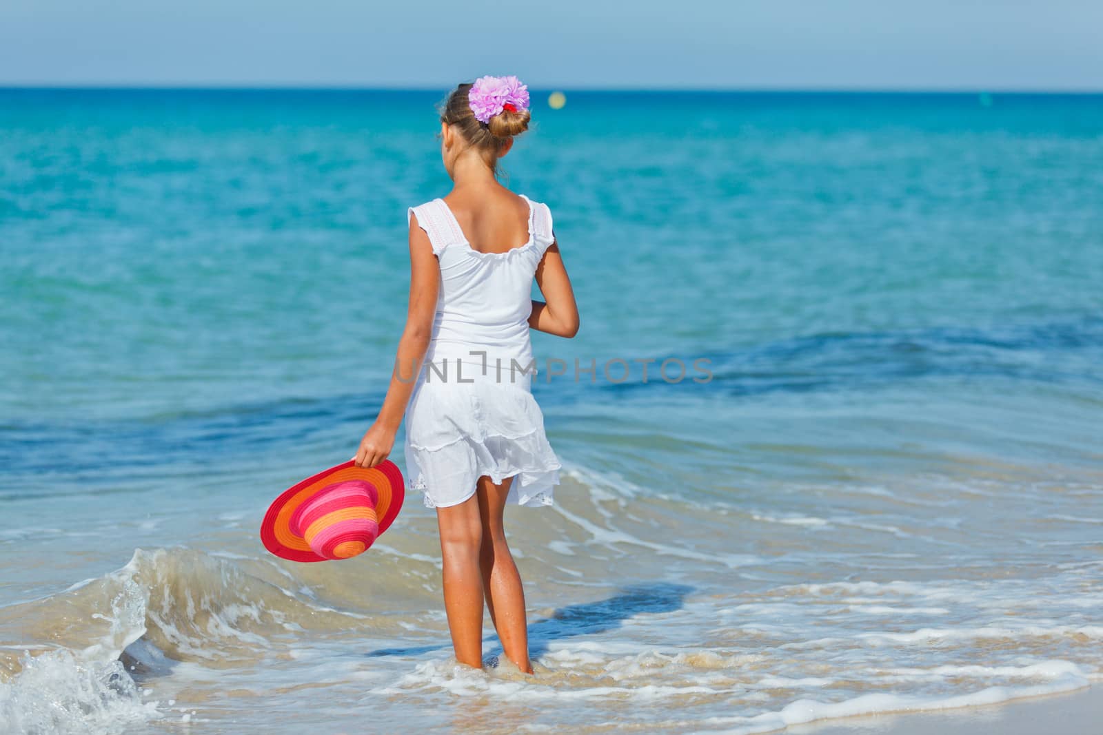 Back view of relaxing beach girl walking with a sun hat at the beach.